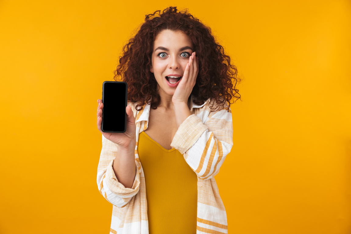 Shocked Curly Haired Woman Holding Showing the Screen of Smartphone